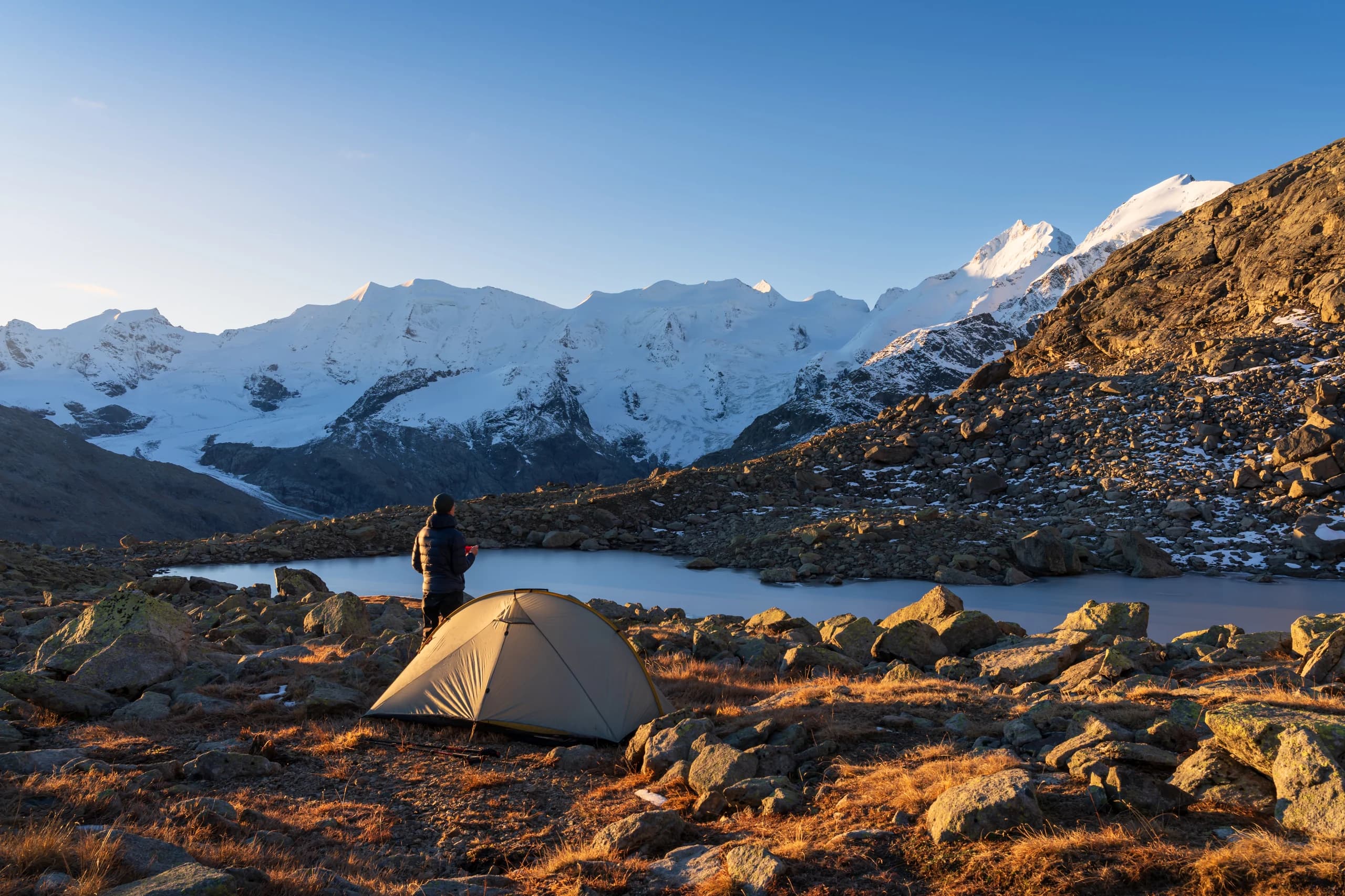 Hiker at sunrise camp by the Bernina range, facing snow-capped peaks